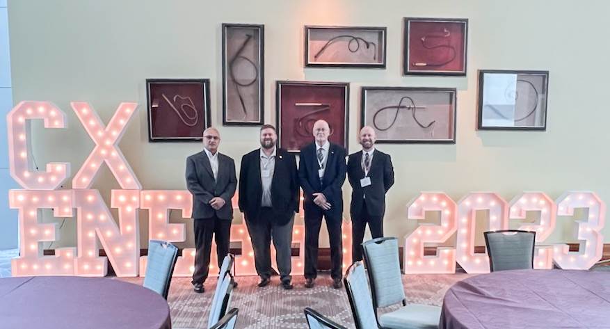 Four men stand next to each other, smiling at the camera, in front of marquee lights that spell CxEnergy 2023
