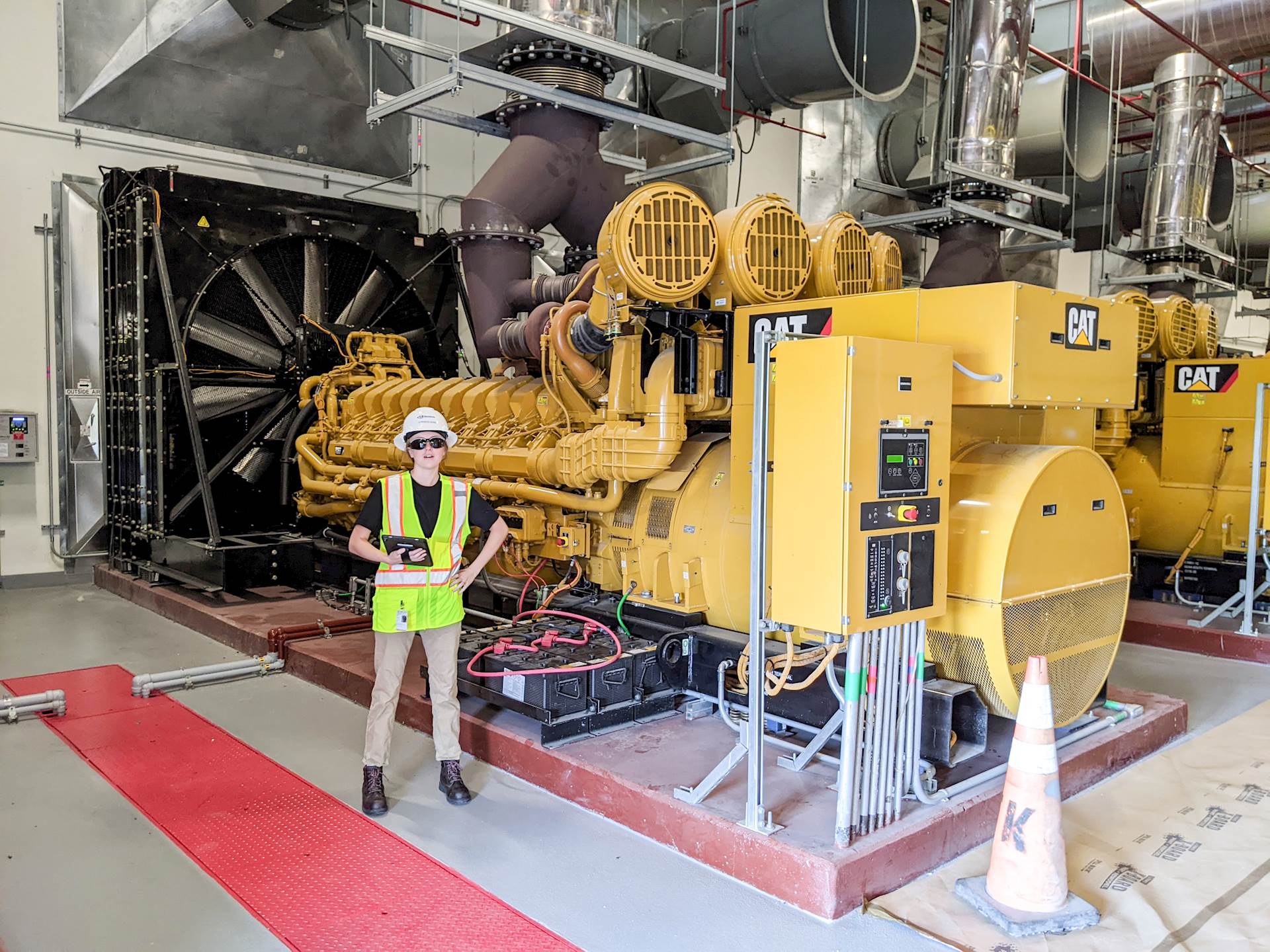 A large generator is behind an intern holding an electronic tablet.