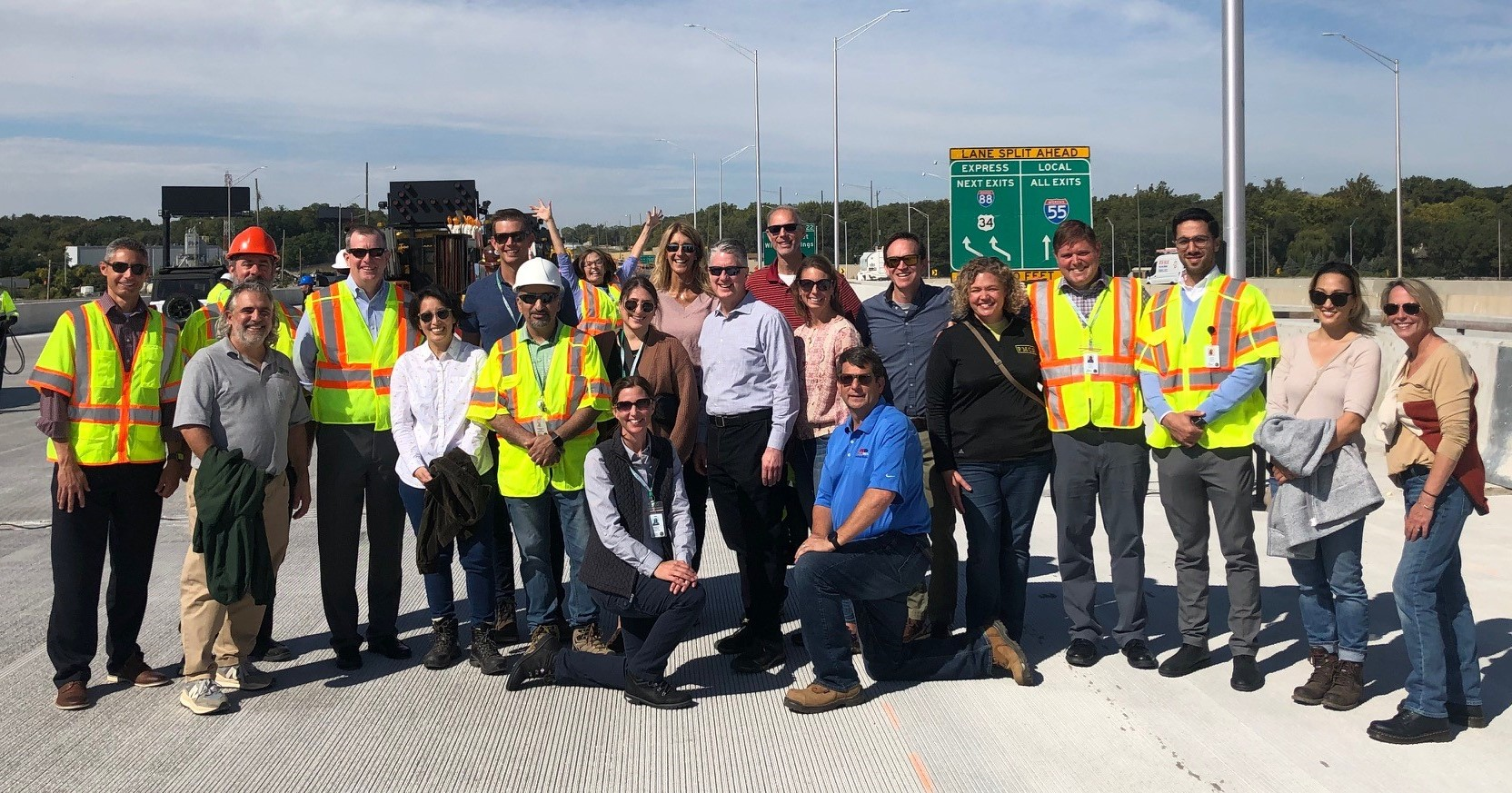 Group of people, several wearing safety vests, posing for a photo on an interstate roadway
