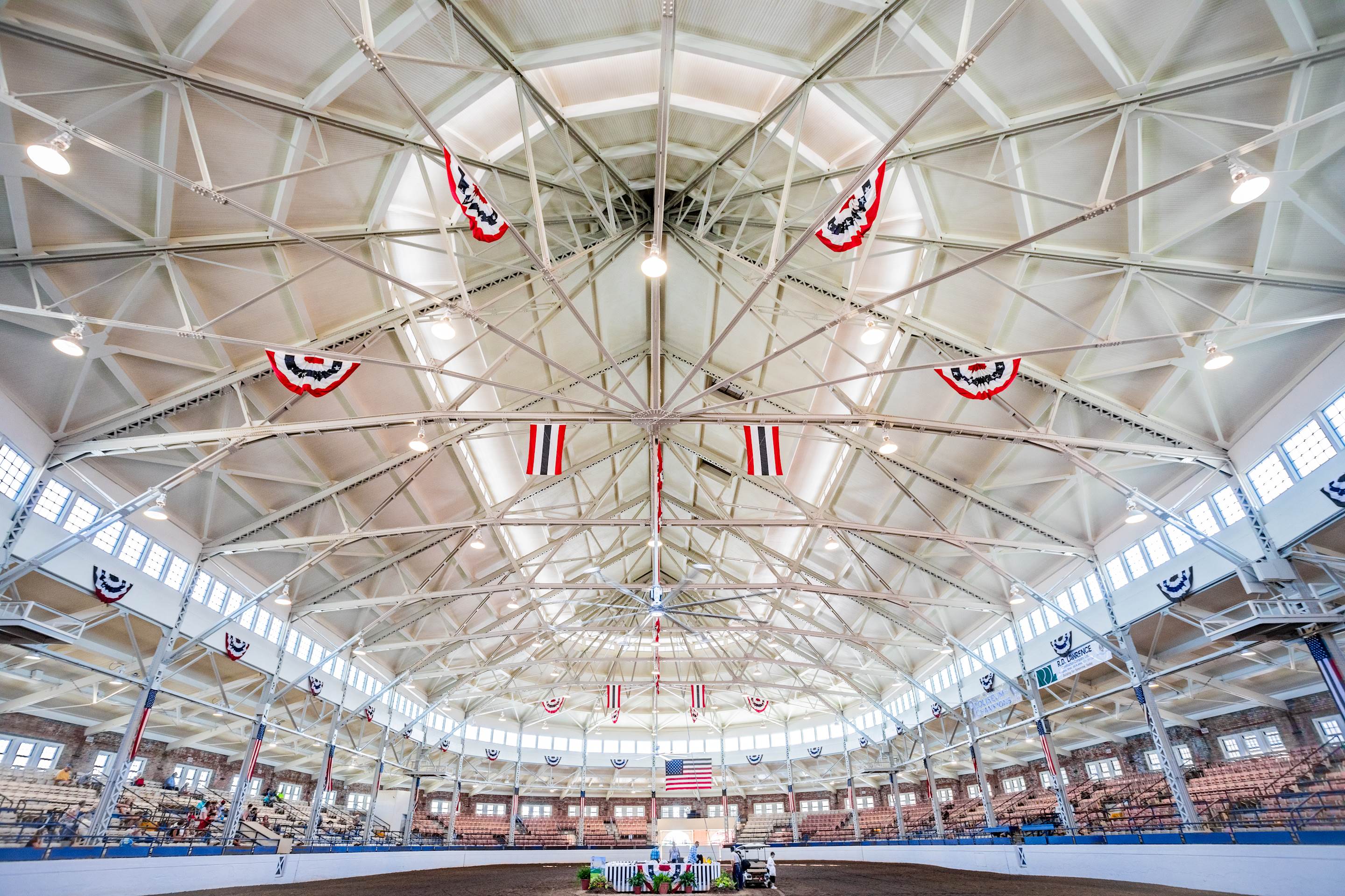 Interior view of the Coliseum during a horse show at the 2019 Illinois State Fair. An oval building with rows of seating around the interior, with a dirt floor and judges' box in the middle.