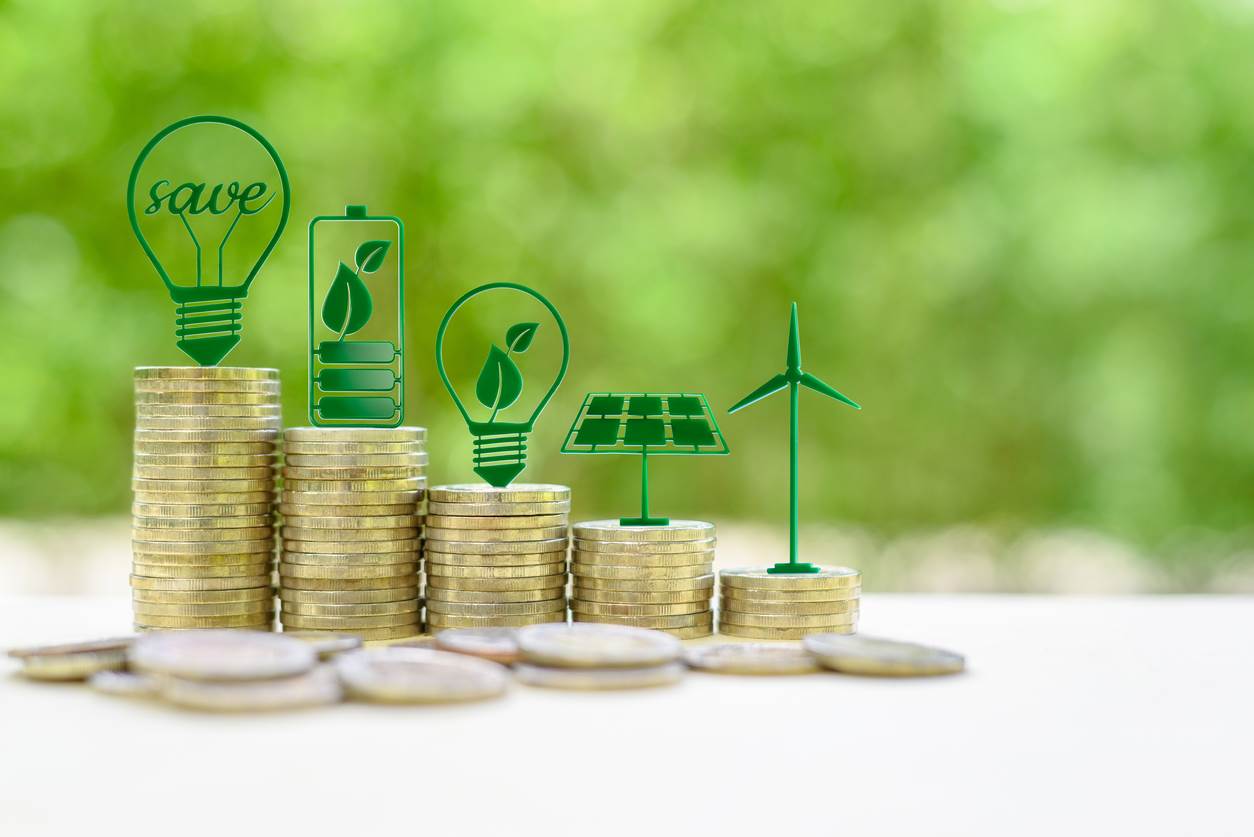 Eco-friendly or sustainable energy symbols of light bulbs, rechargeable battery, solar cell panel and wind turbine atop five coin stacks