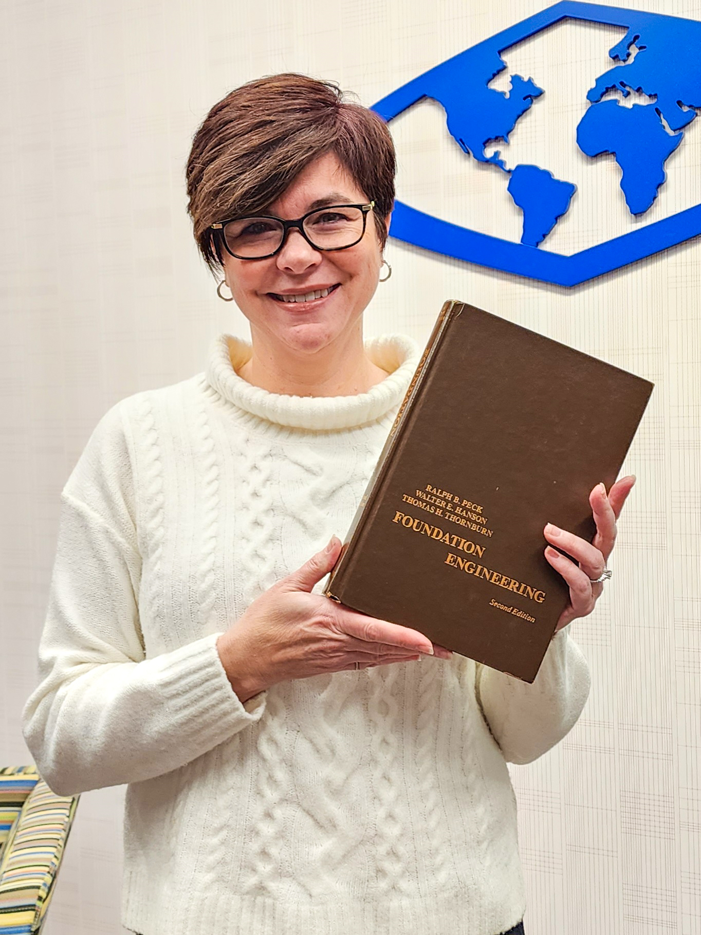 Photo of woman in white sweater with short brown hair holding book