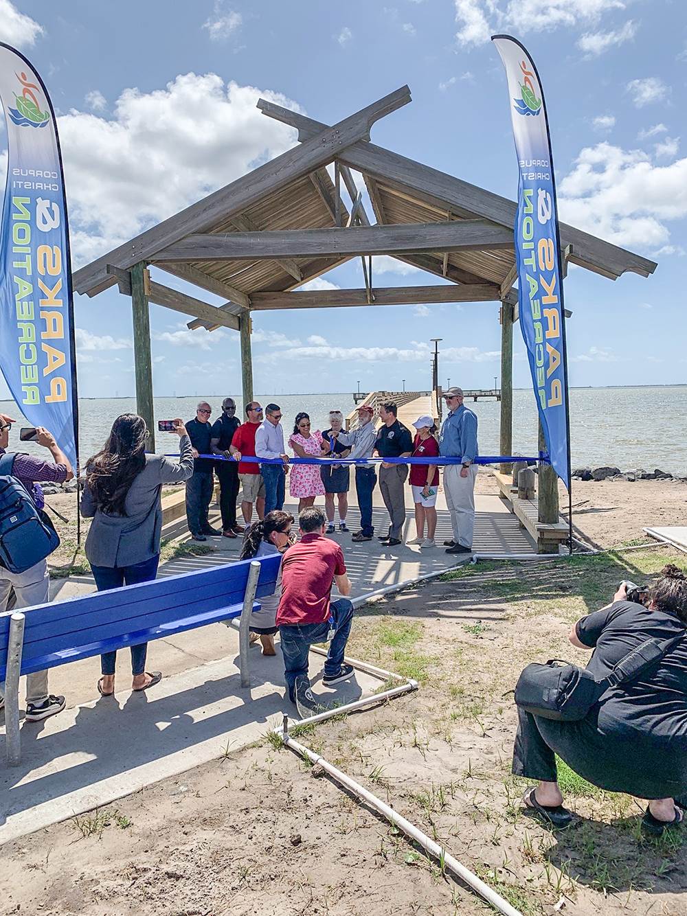 a group of  people cutting the ribbon on a wooden pier project in corpus christi, texas