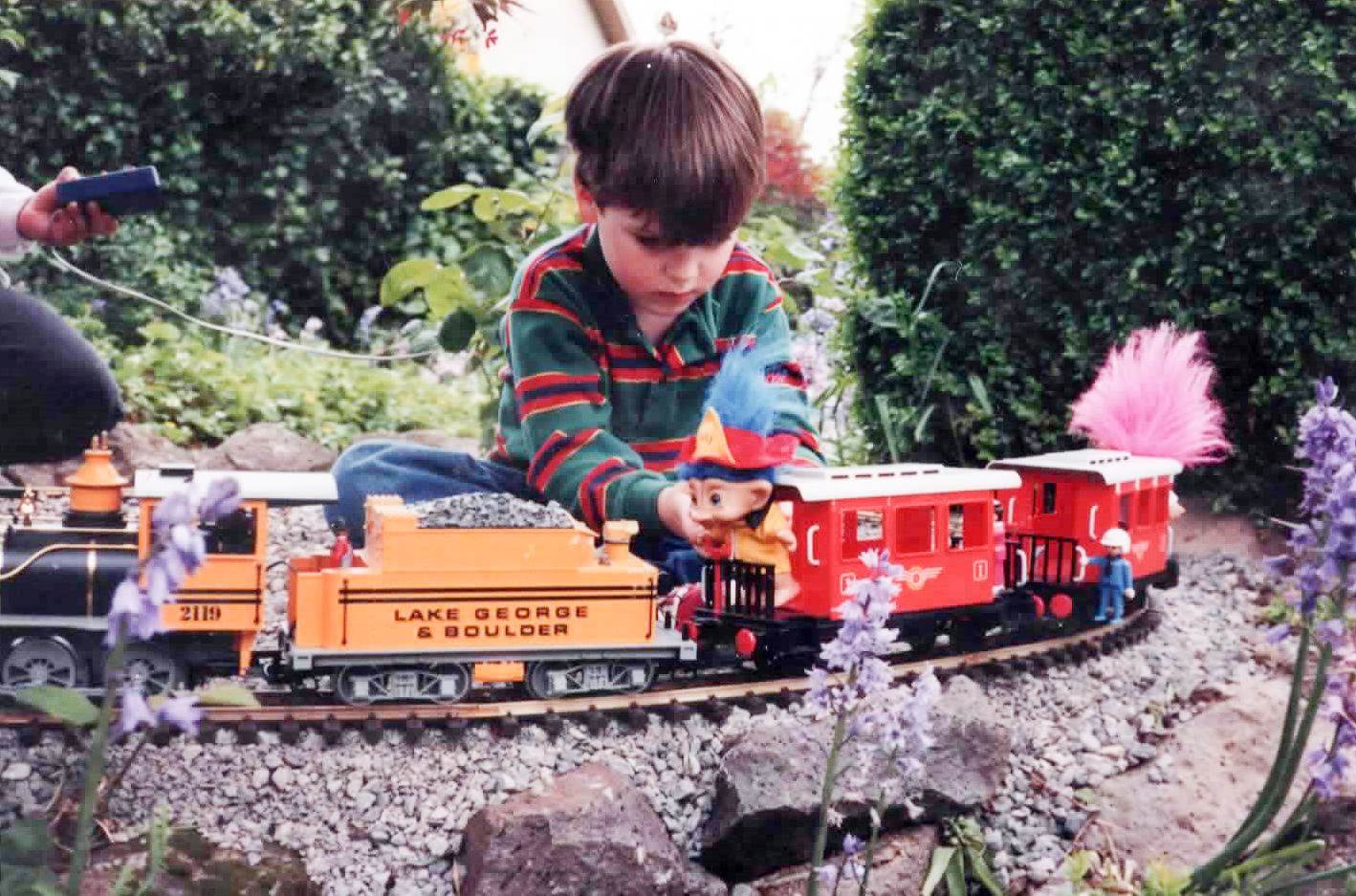 Tristan Rickett, as a child, plays with a model train and Troll dolls outside.