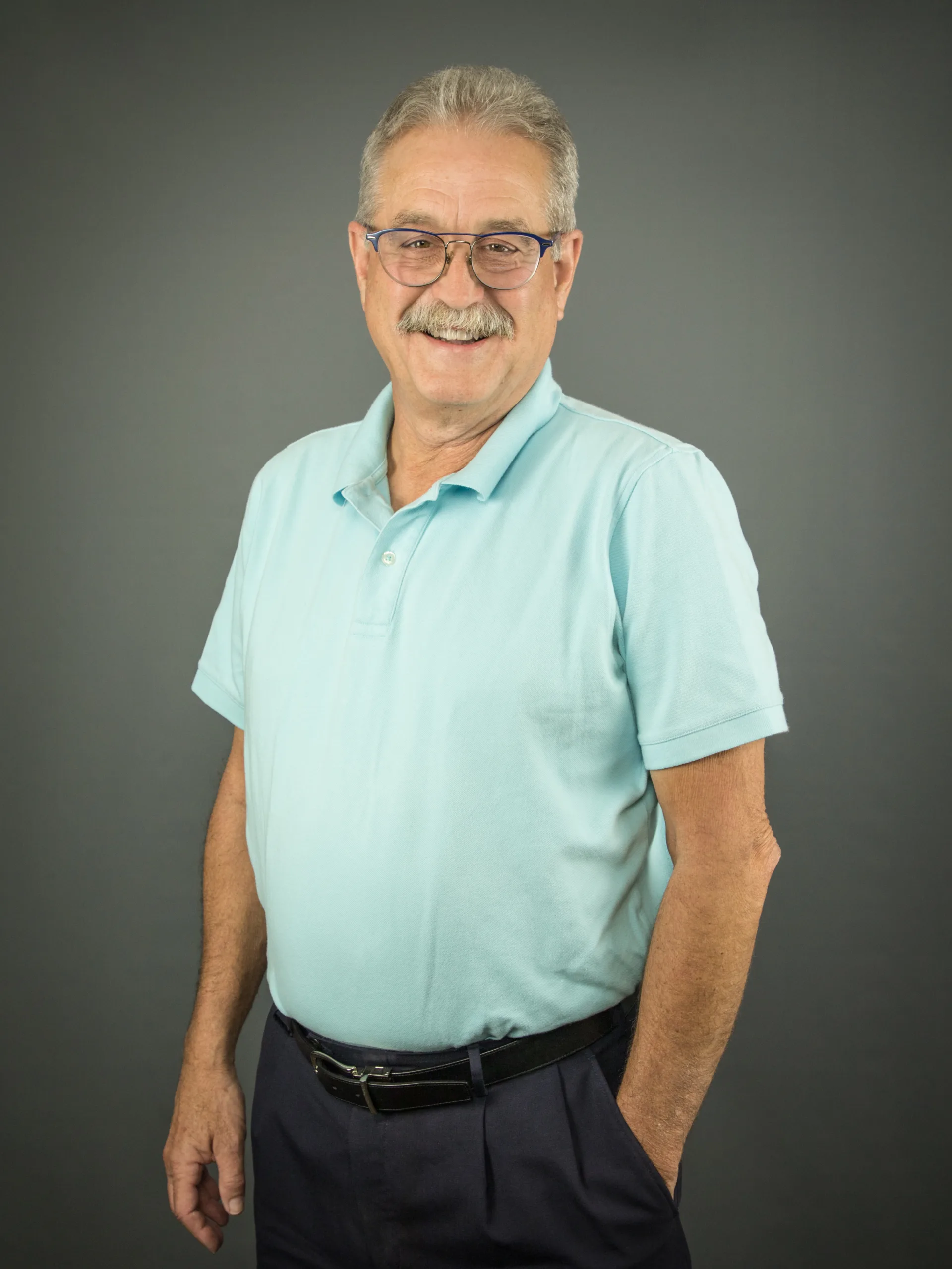 Portrait of Rhon Hasenyager, standing and smiling at camera, his hand in his pocket