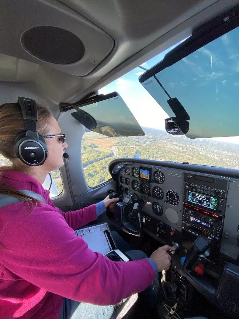 Side view of Susan Zellers flying a plane with ground view in background