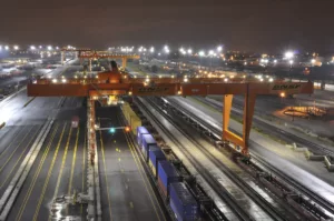 Large orange intermodal terminal at night with lights in background and train in foreground