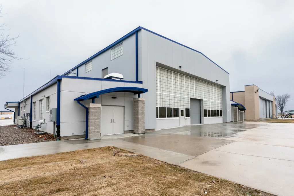 Large military building, gray with royal blue trim, surrounded by concrete, grass and gravel wet from rain, gray sky in background