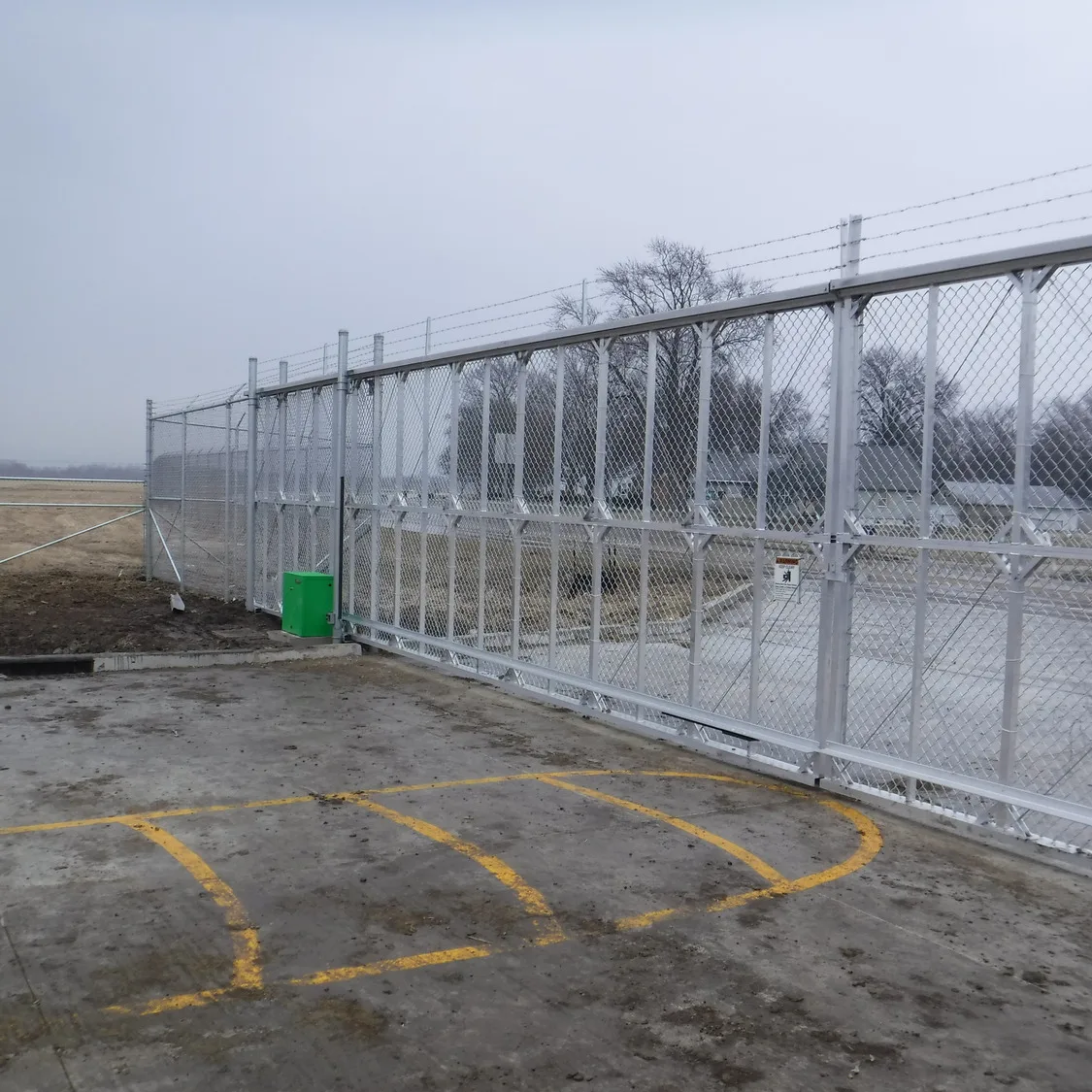 Security fence with muddy pavement in foreground and roadway in background
