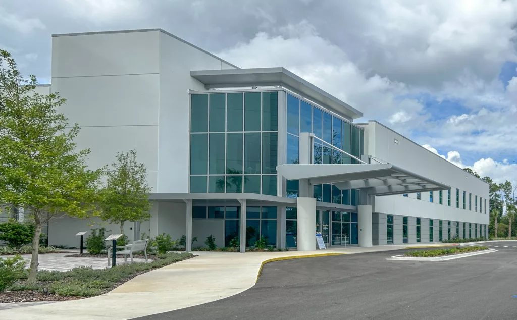 Healthcare building in shades of gray and blue with trees and parking lot surrounding