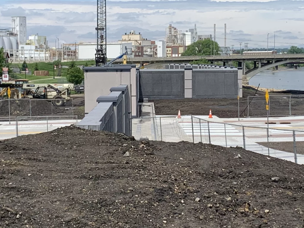 Floodwall with blue sky, bridge, river and factory in background