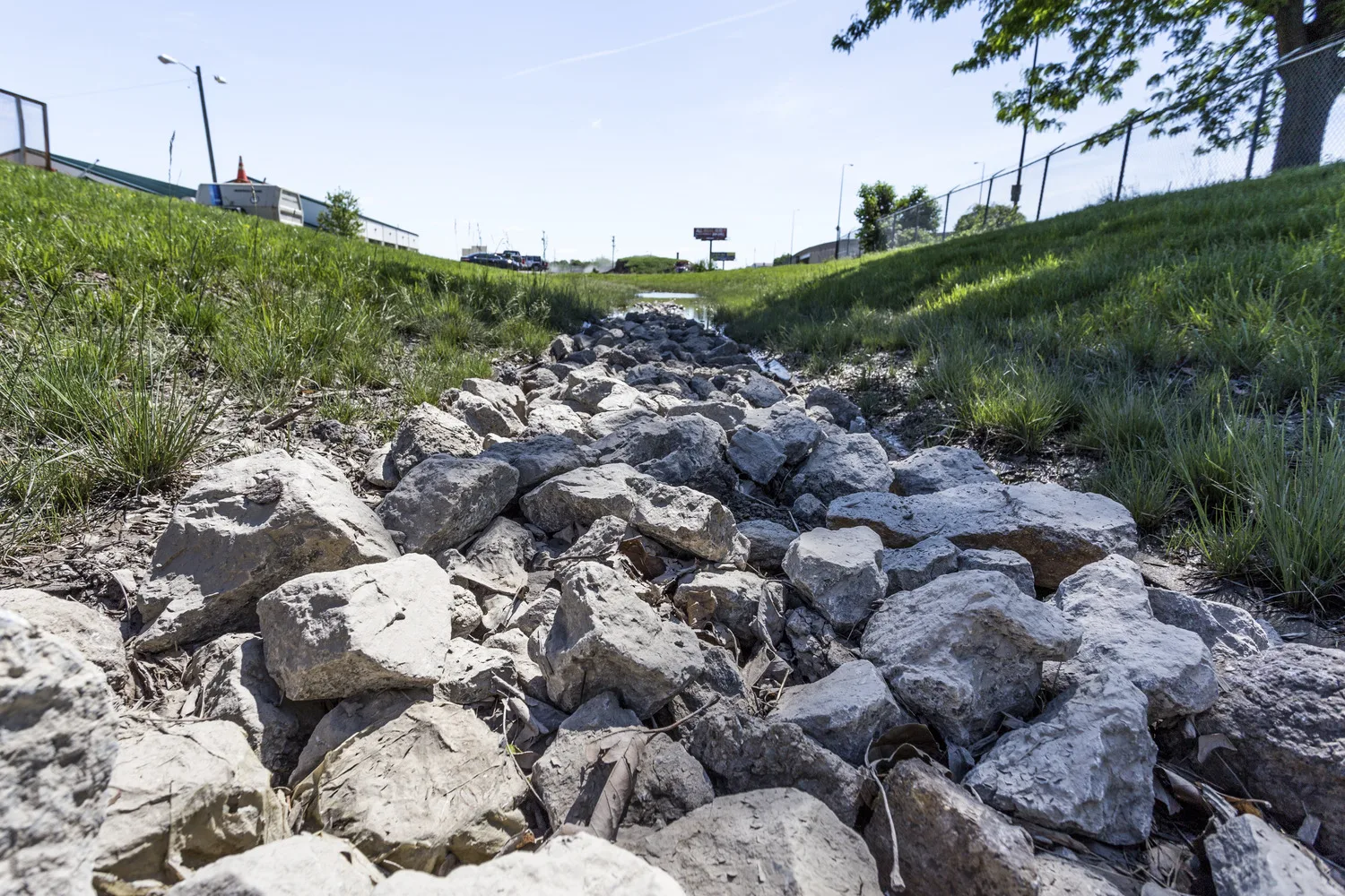 Rocks in a ditch are surrounded by green grass and a fence on one side