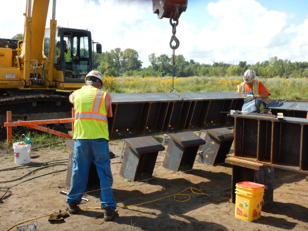 Men in safety gear working on transmission tower foundation with yellow construction machinery in background