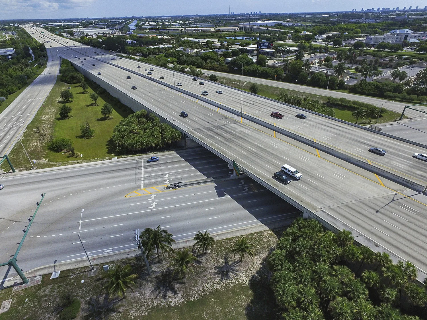 Aerial view of roadway running under interstate with trees, buildings and blue sky in background