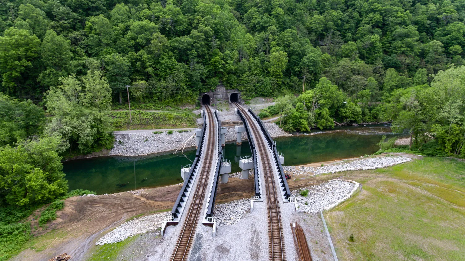Aerial view of rail bridge with two parallel tracks over stream leading into tunnels