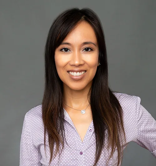 Woman with long, dark hair in light purple shirt with dark gray background