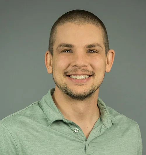 Man with close-cropped black hair, a green heathered polo shirt and light beige background