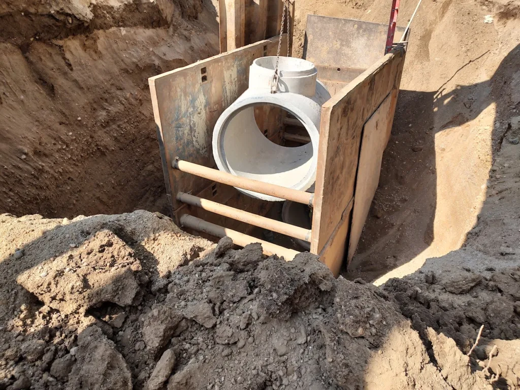 Construction scene with large white pipe in wooden surround, being buried in dirt