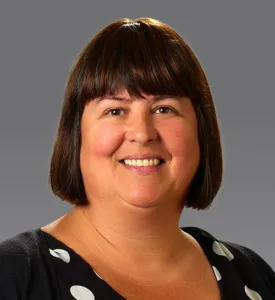 Woman with short dark hair and bangs, wearing black dress with large white polka dots, with dark gray background