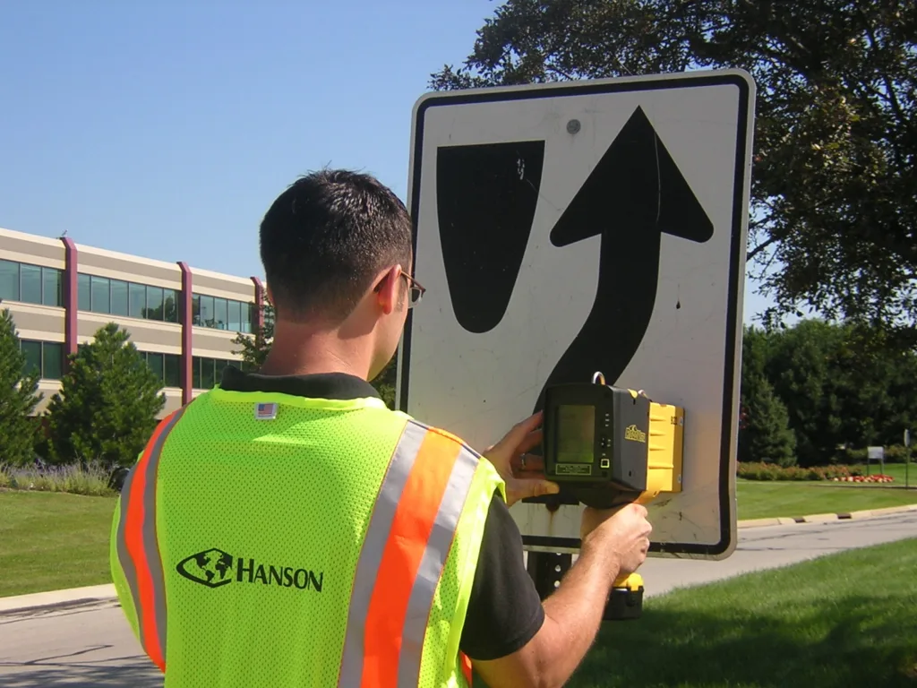 man in neon yellow and orange safety vest using surveying device on street sign with blue sky in background