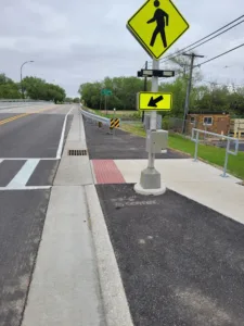 ADA-compliant crosswalk with neon-yellow sign and roadway off to left