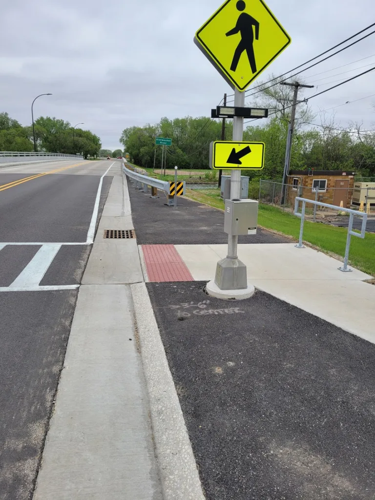 ADA-compliant crosswalk with neon-yellow sign and roadway off to left
