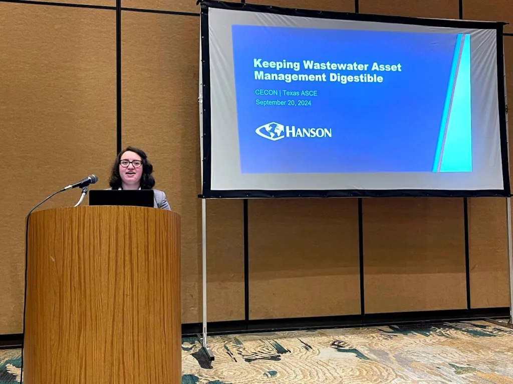 Michelle Alvarez speaks from behind a lecturn with a screen behind her that says, "Keeping wastewater asset management digestible."