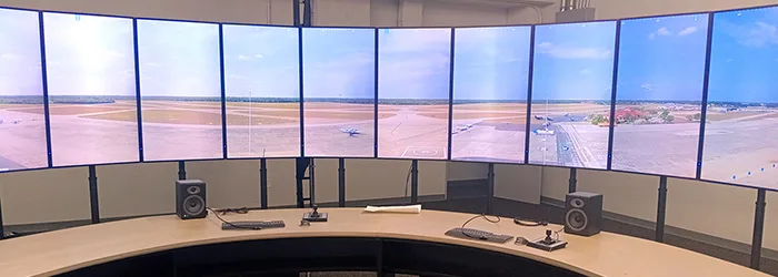 View of the inside of a remote control tower control center, with 10 vertical monitors showing an airfield