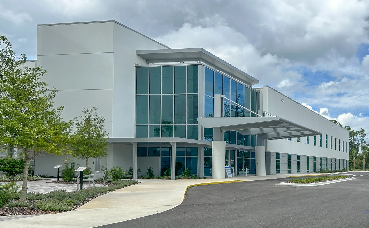 Exterior of a hospital with many mirrored windows, palm trees and blue sky with clouds