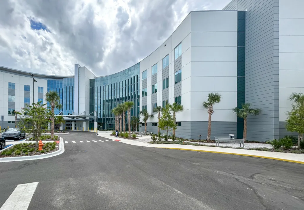 Exterior of a hospital with many mirrored windows, palm trees and blue sky with clouds