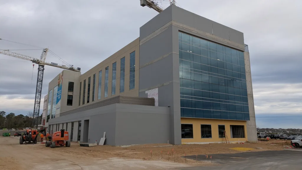 Medical building under construction, with equipment, two cranes and parked cars surrounding
