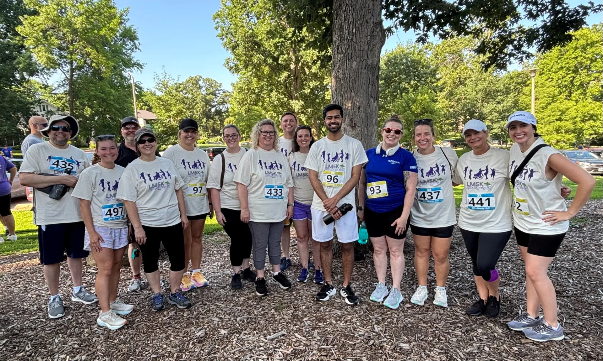 Group photo of Hanson employees in park setting wearing cream-colored shirts and race numbers
