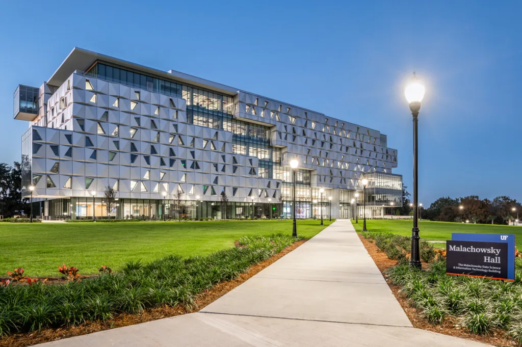 Exterior view of building at dusk; silver panels and two banks of windows; blue sky in background and green grass in foreground