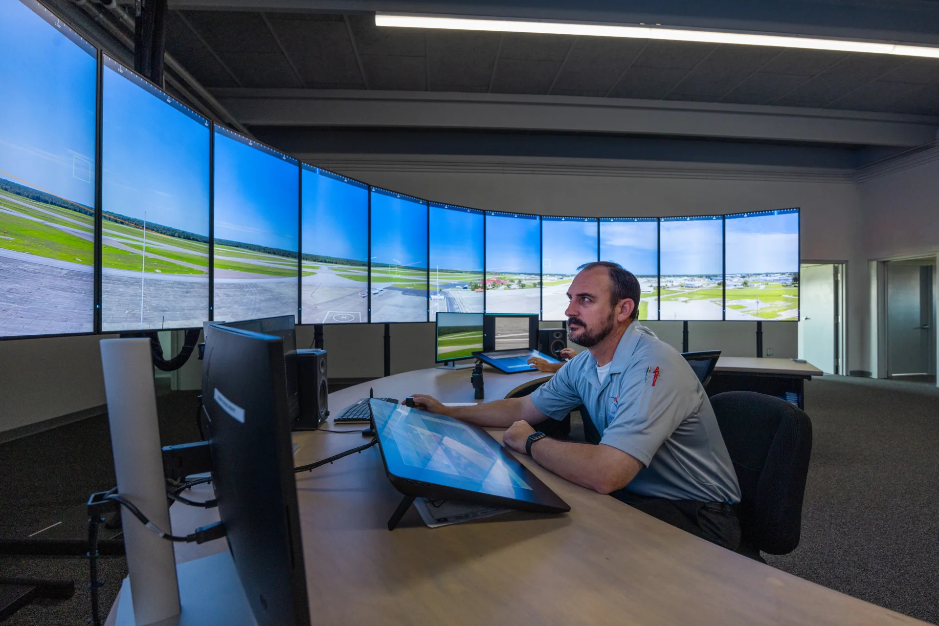 View of the inside of a digital tower control center, with 10 vertical monitors showing an airfield and man working at desk