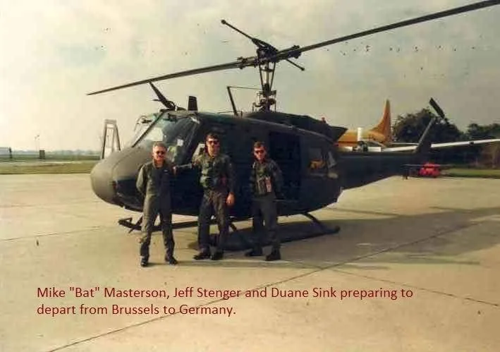 Three men in military uniforms standing in front of helicopter on runway at airport