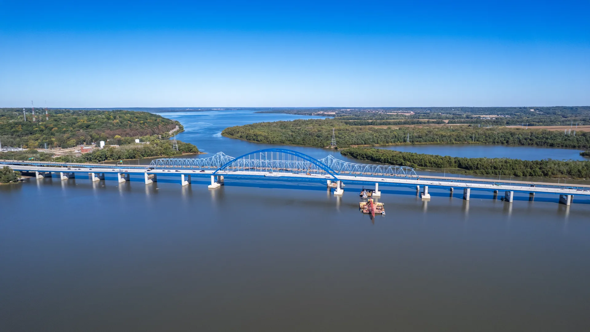 Aerial shot of two blue bridges side by side over river with bright blue sky overhead
