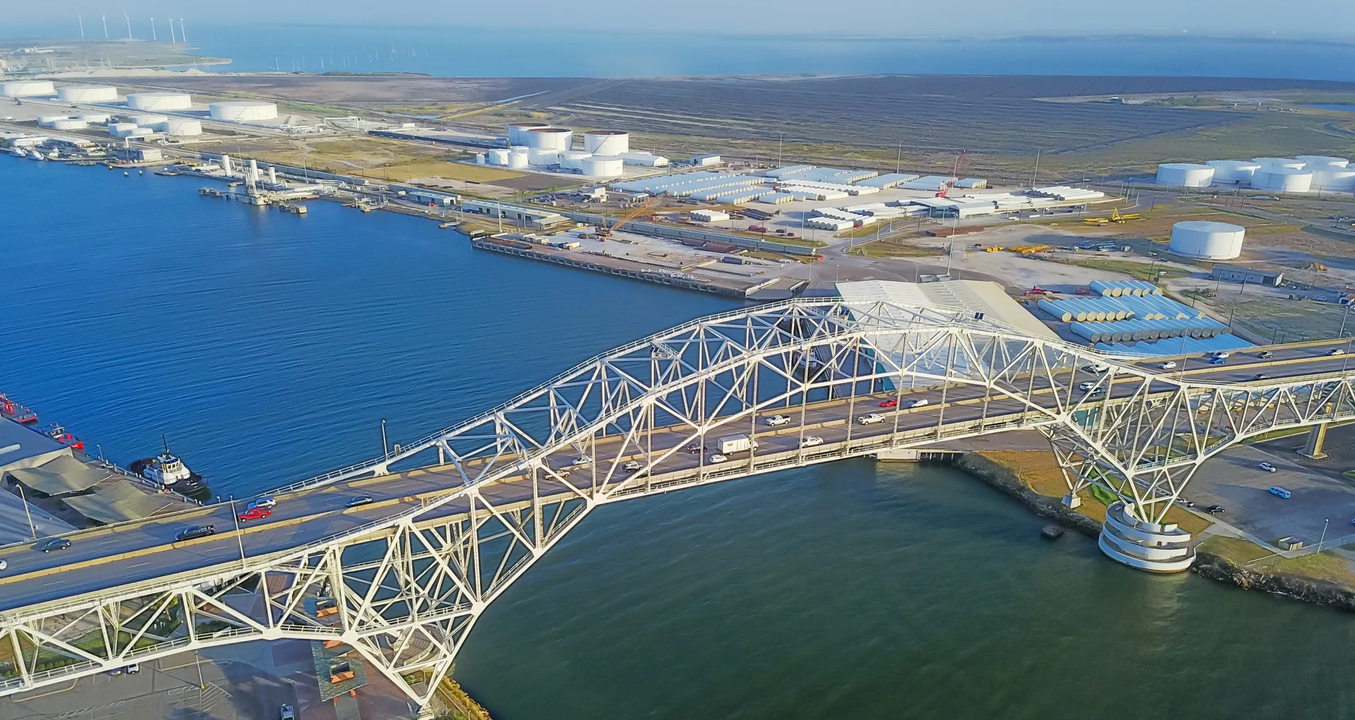 Vintage tone aerial view of Corpus Christi Harbor Bridge with row of oil tanks at far right in distance. A through arch bridge crosses the Corpus Christi Ship Channel
