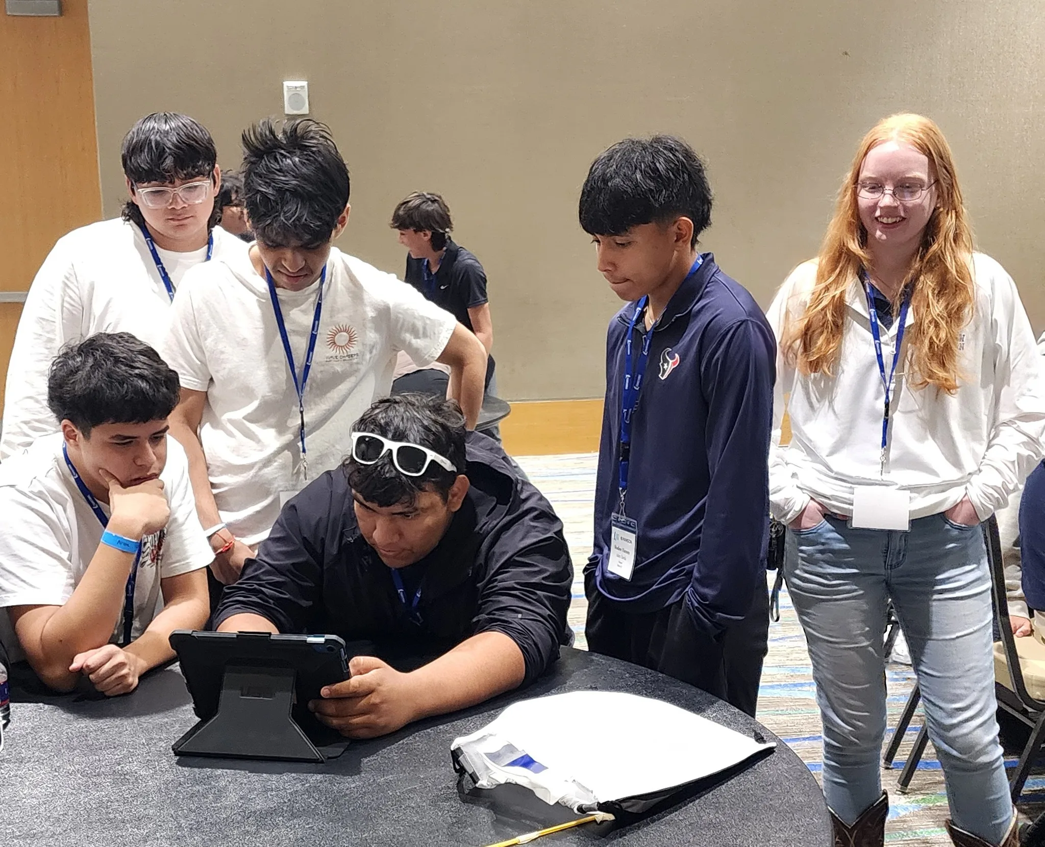 Five students and a Hanson employee sit and stand around a table, looking at a tablet