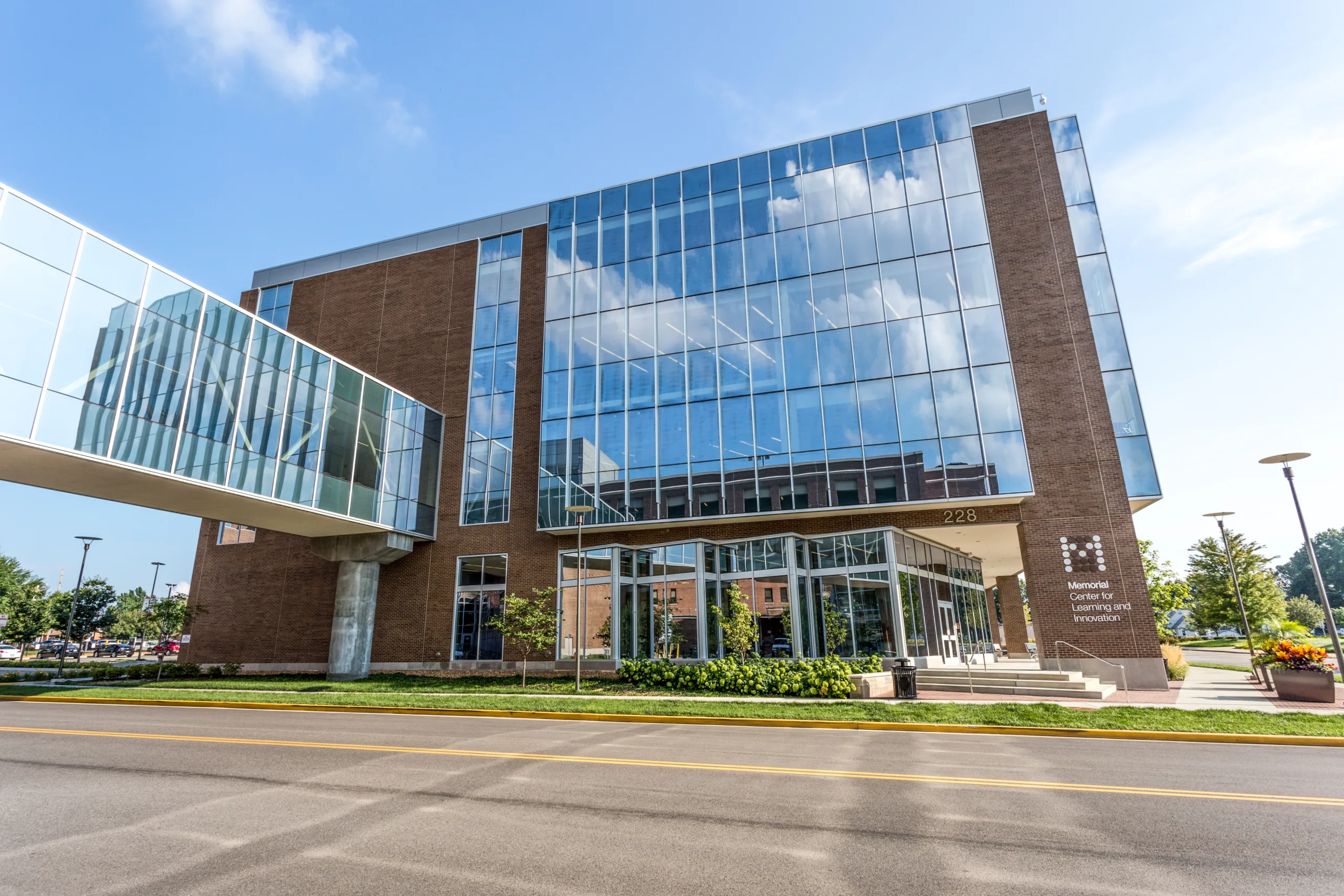 Close-up photo of medical building with reflective exterior and brick, pedestrian bridge extending from left side and Memorial Center for Learning and Innovation sign at right, near steps