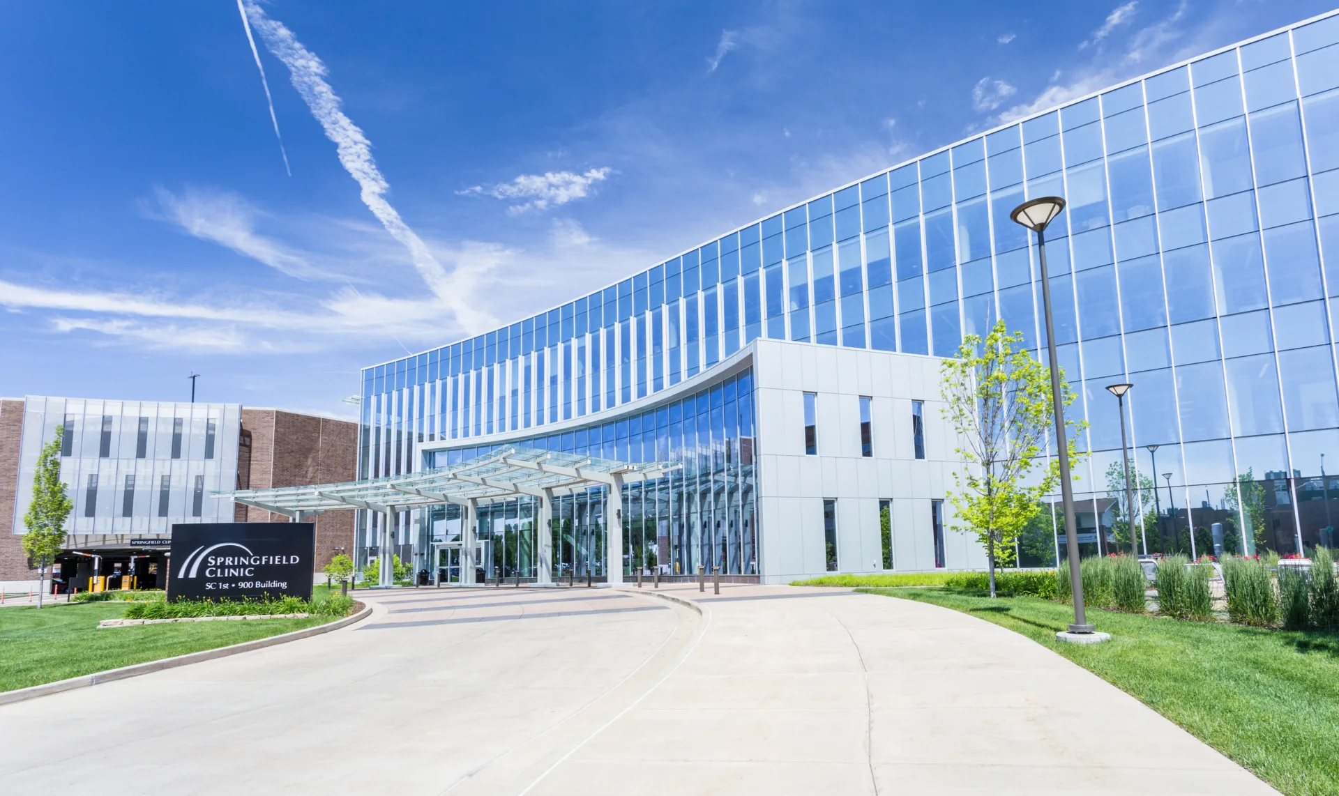 Close-up exterior shot of medical building with reflective windows and modern-looking canopy over entrance on circle drive and sign in front reading, "Springfield Clinic"
