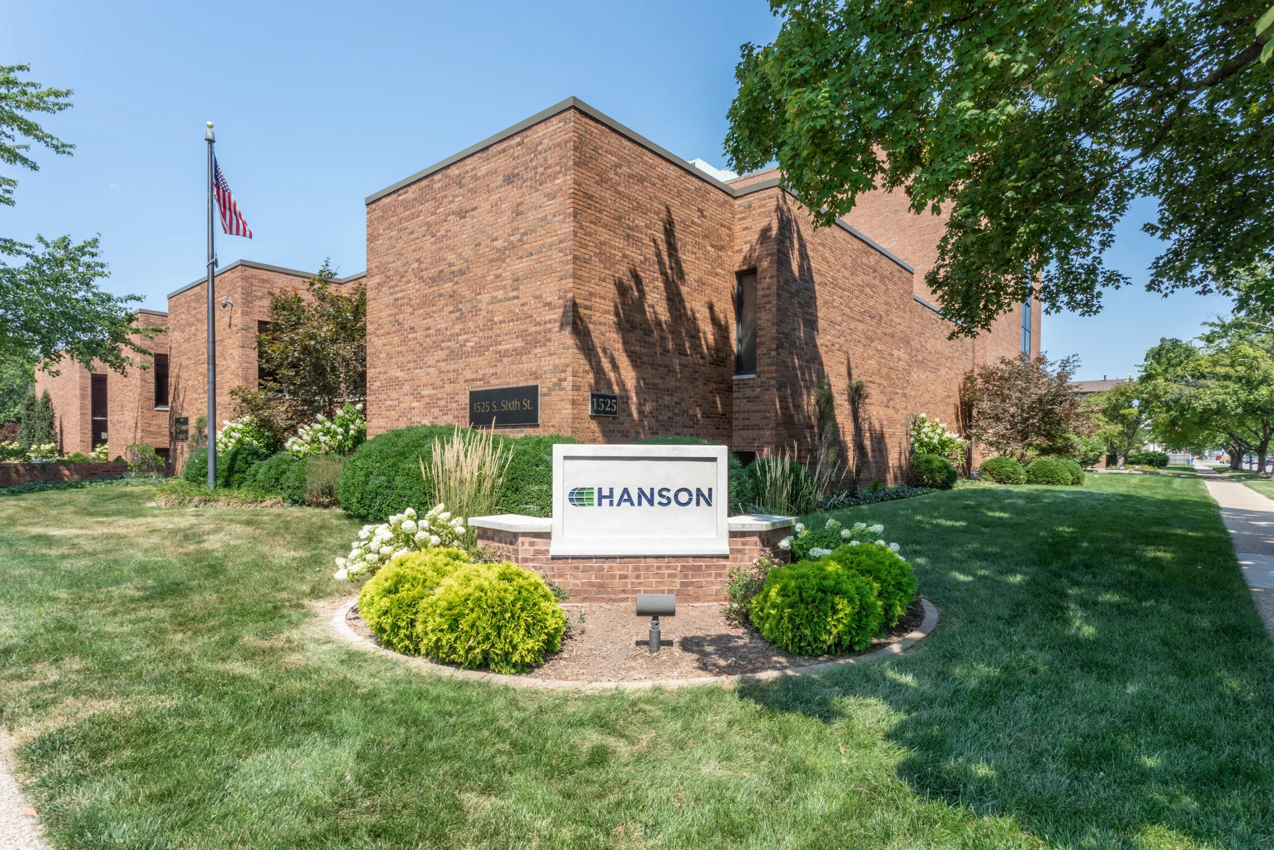 Exterior photo of red brick building with stone sign featuring Hanson's new green and blue logo, surrounded by green grass and trees