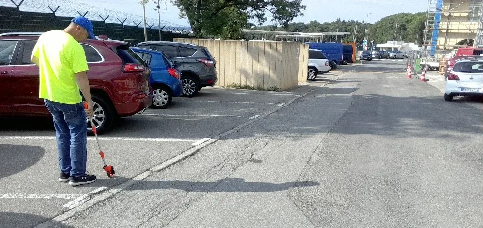 image of a man in a neon yellow shirt, jeans and black sneakers conducting a survey with an orange and silver wand behind three parked cars along a roadway