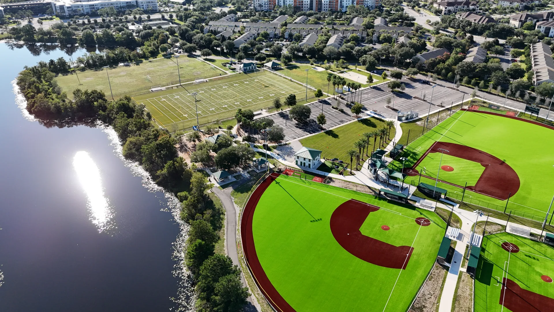 Aerial photo of a sports park with football field at top, parking lot in center, baseball fields in right corner and large retention pond at left