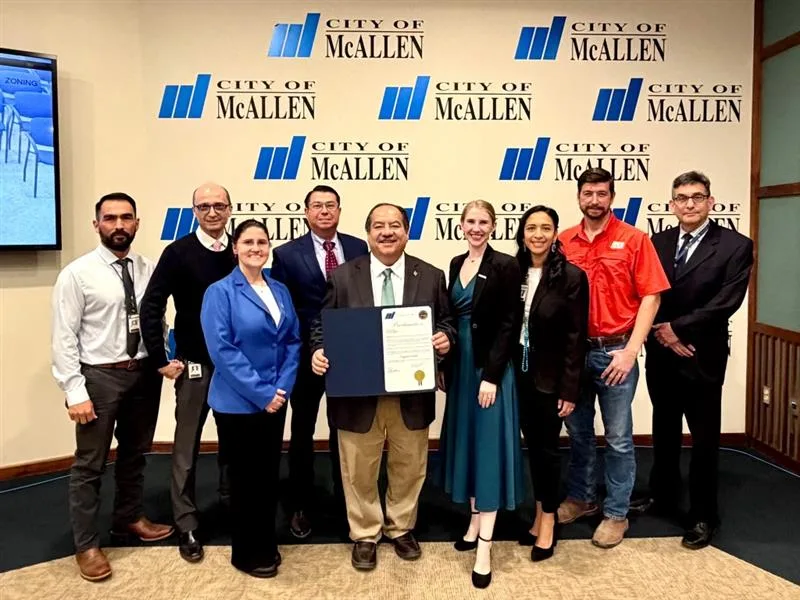 Group of nine people in front of backdrop with "City of McAllen" logo repeating