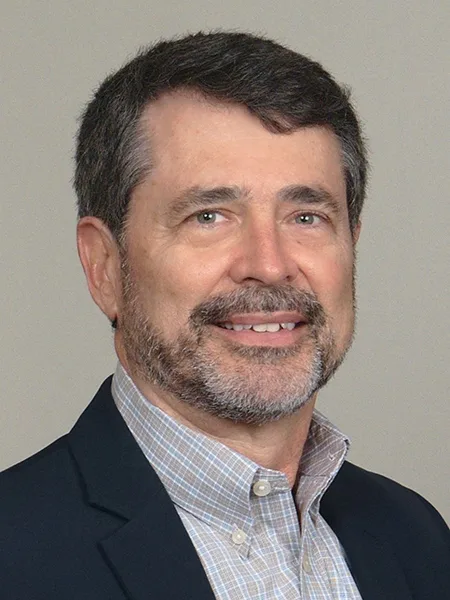 headshot of Eric Menger wearing light-colored collared shirt and black suit jacket