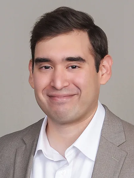 headshot of gerry rangel wearing white collared shirt and light gray jacket on light gray background