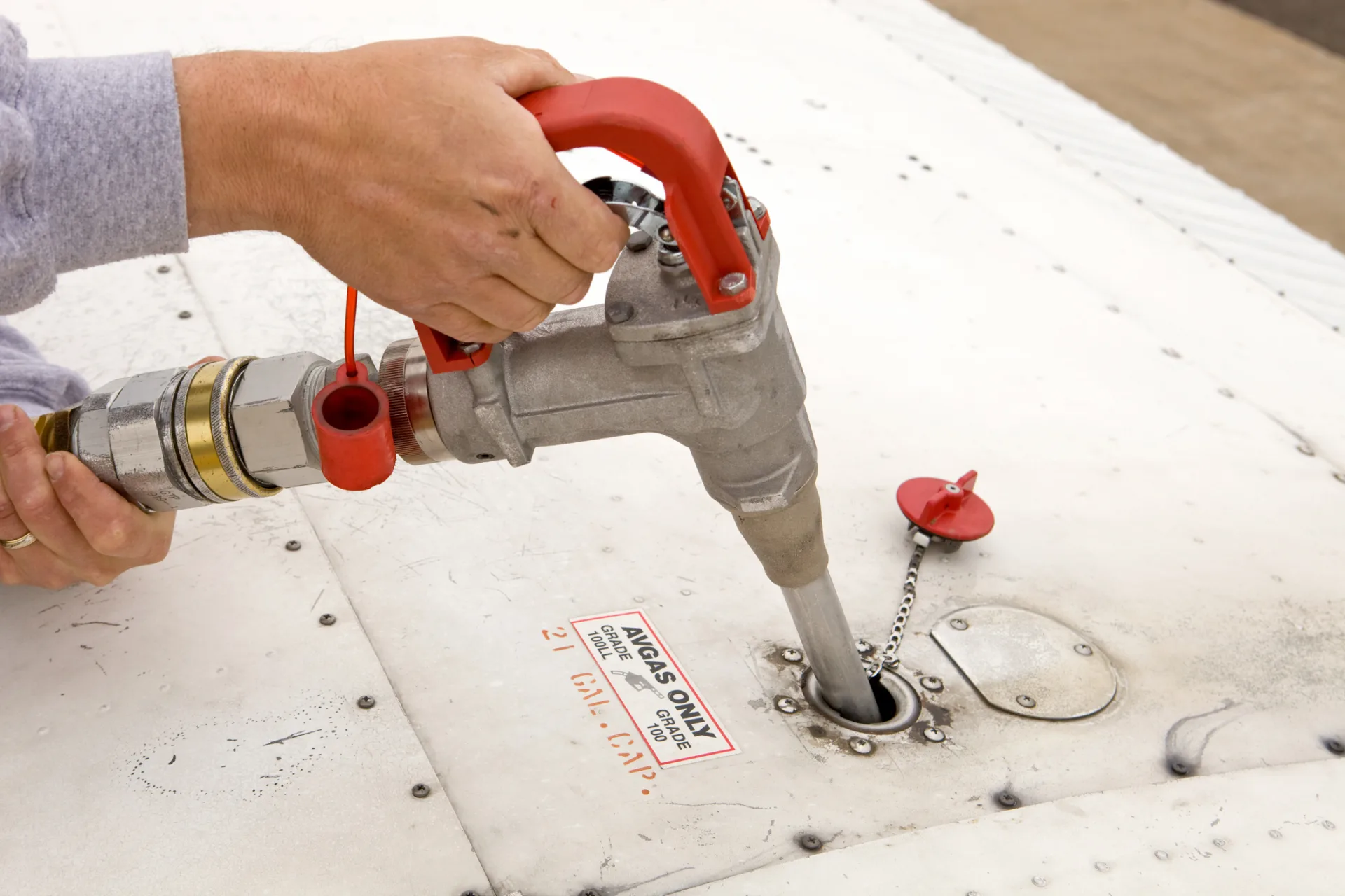 Close-up stock image of gasoline pump being inserted into airplane wing