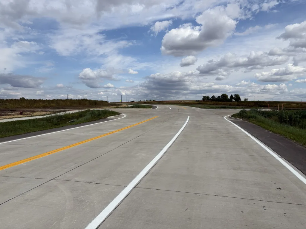 Ground view of a new roadway with additional roadways angling to the left and right; blue sky with puffy, white clouds overhead