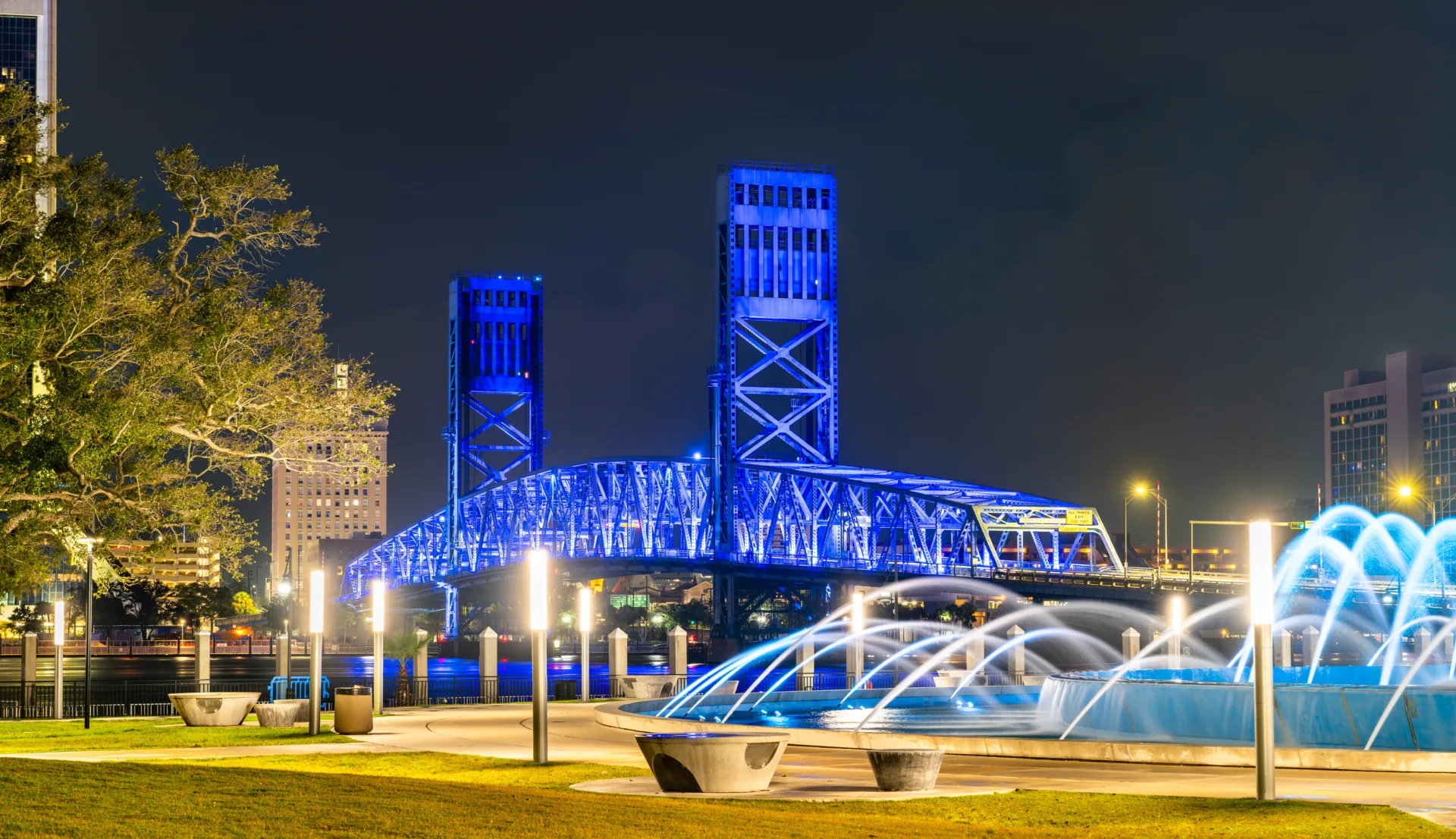 Beautiful night view of the illuminated Main Street Bridge and Friendship Fountain in downtown Jacksonville, Florida, with city lights and urban architecture.