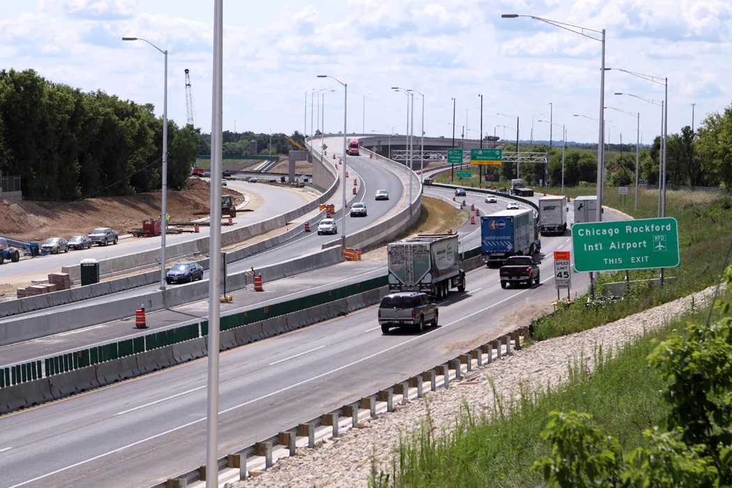 Photo of busy urban expressway with cars and trucks on three roadways and fourth roadway under construction at left.
